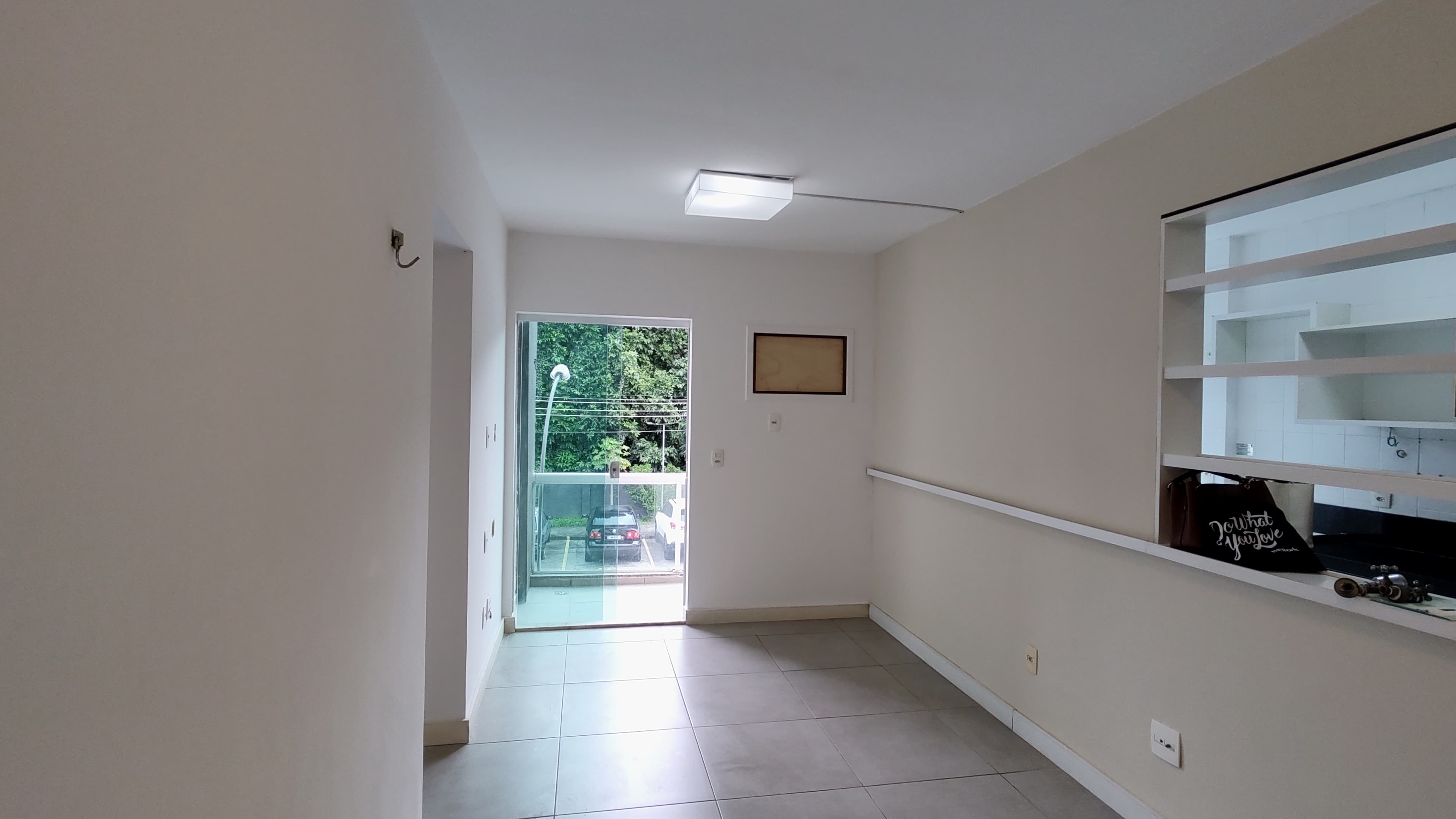 Sala vazia com piso de cerâmica, parede branca e janela tipo passa-pratos integrada para a cozinha.