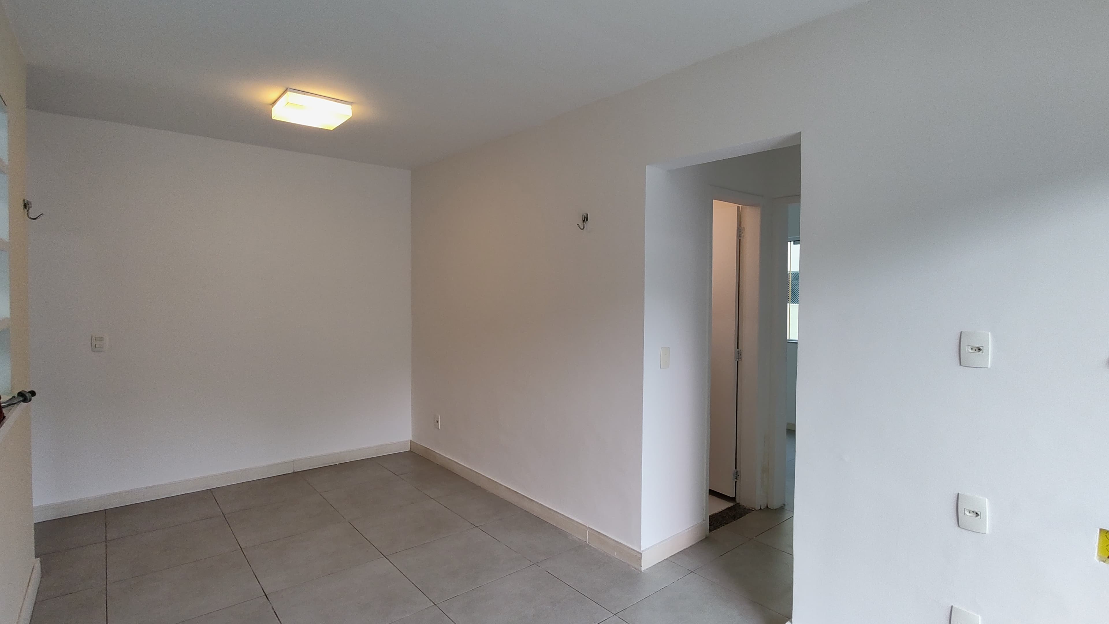 Sala vazia com paredes brancas, piso em cerâmica cinza e luminária de teto.