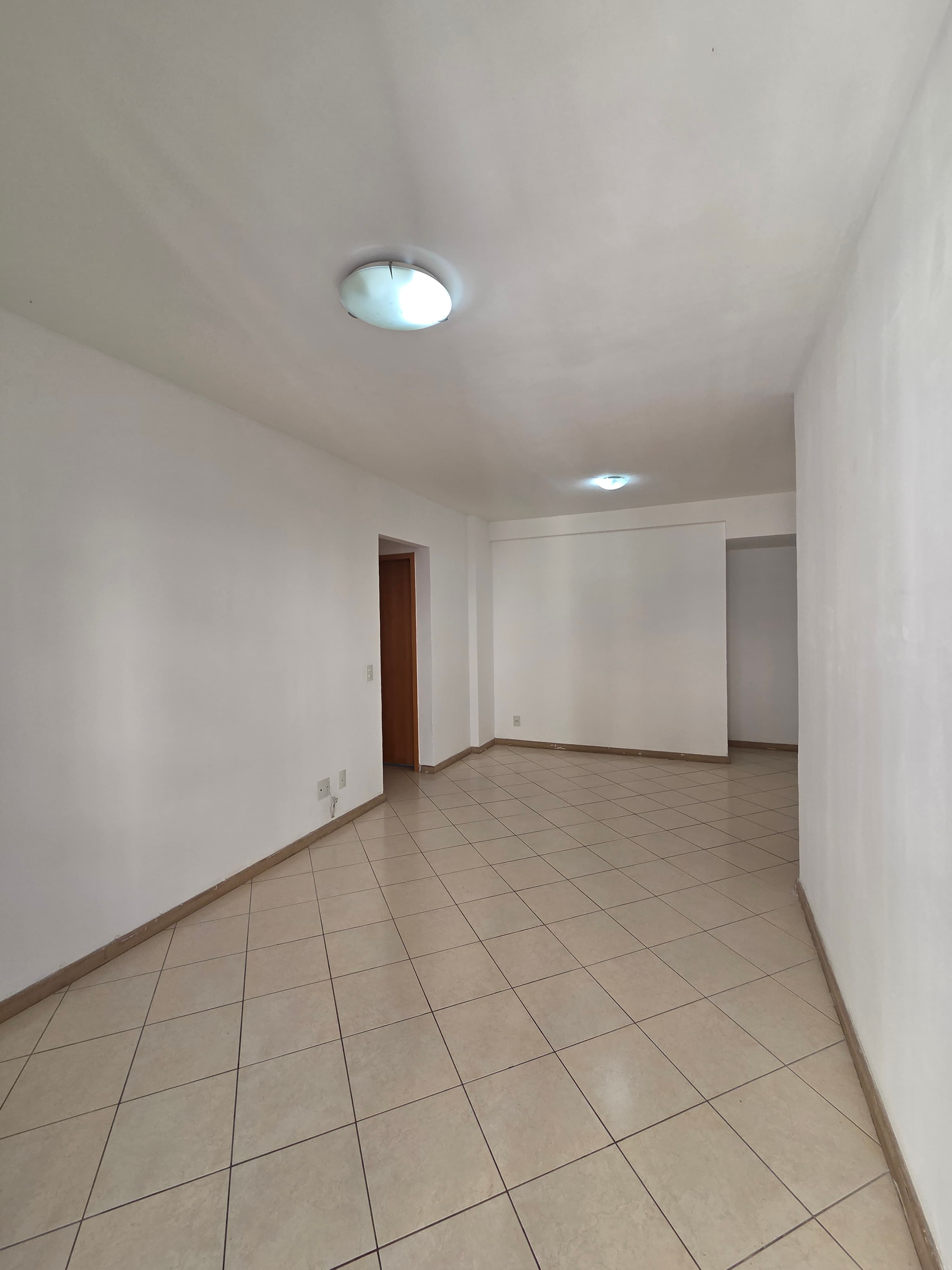 Sala ampla e vazia com paredes brancas e piso em cerâmica clara.