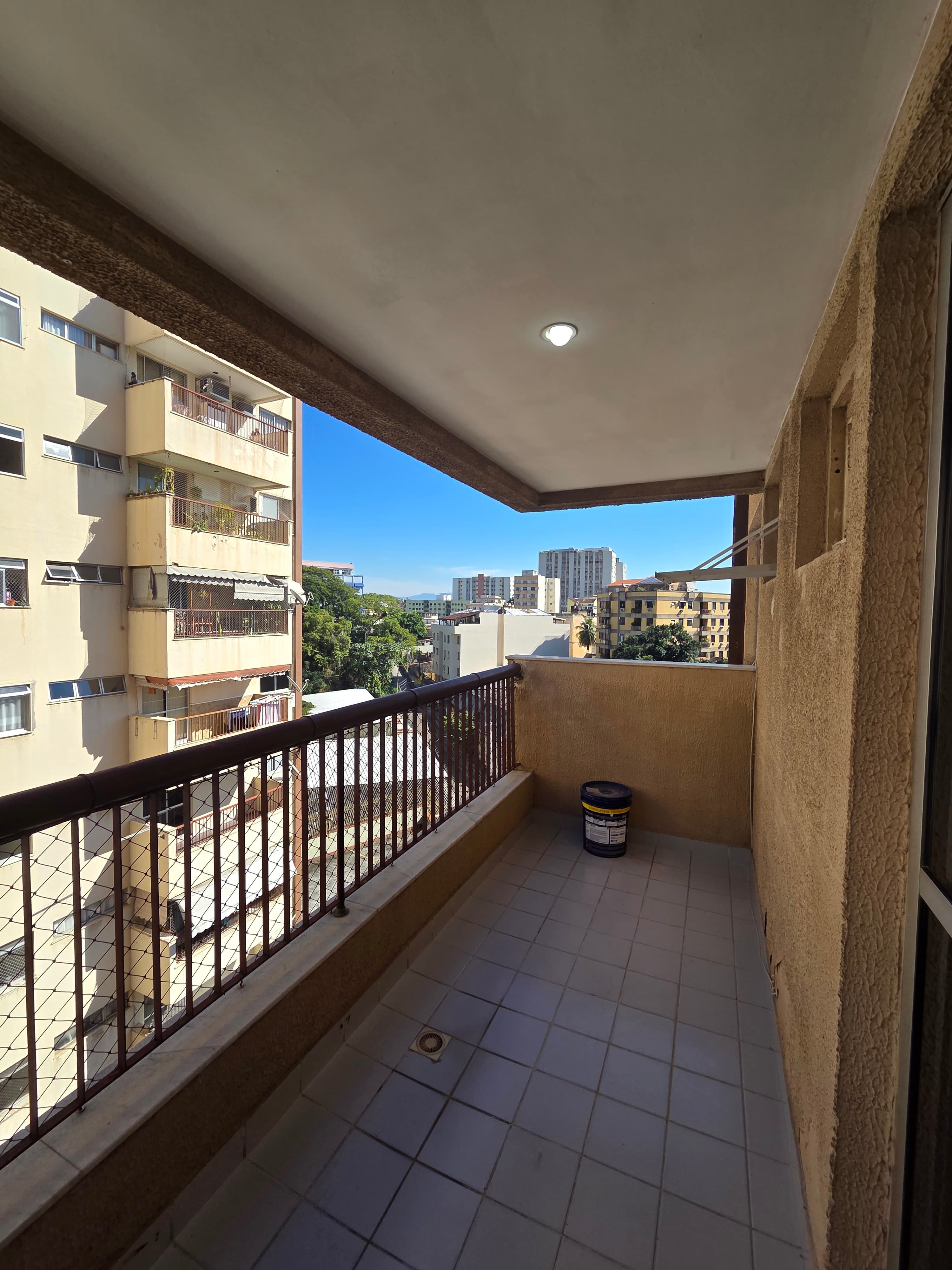Varanda com piso de cerâmica clara, grade de proteção e vista para prédios vizinhos.