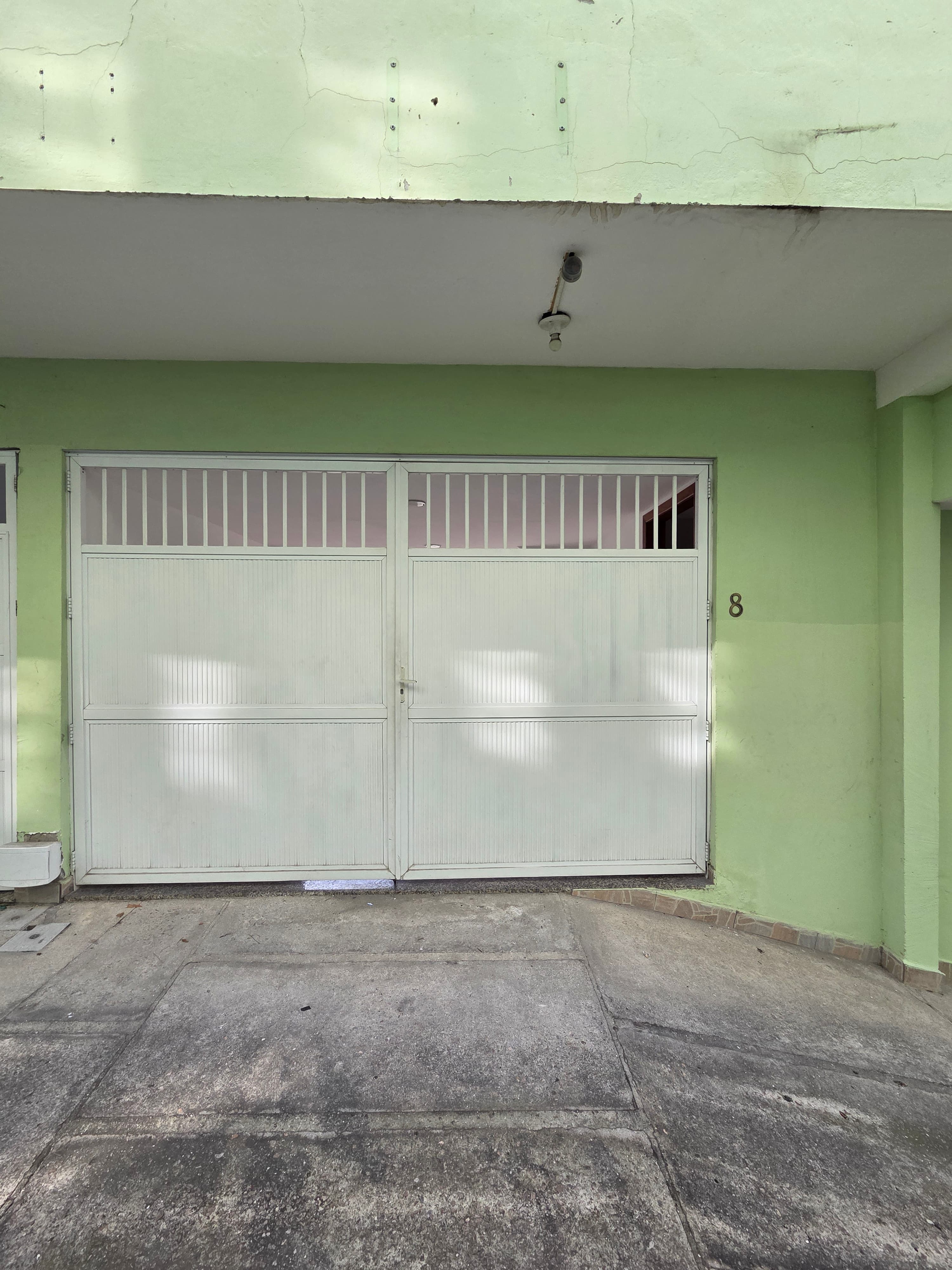 Fachada com portão de garagem branco e paredes pintadas em verde claro