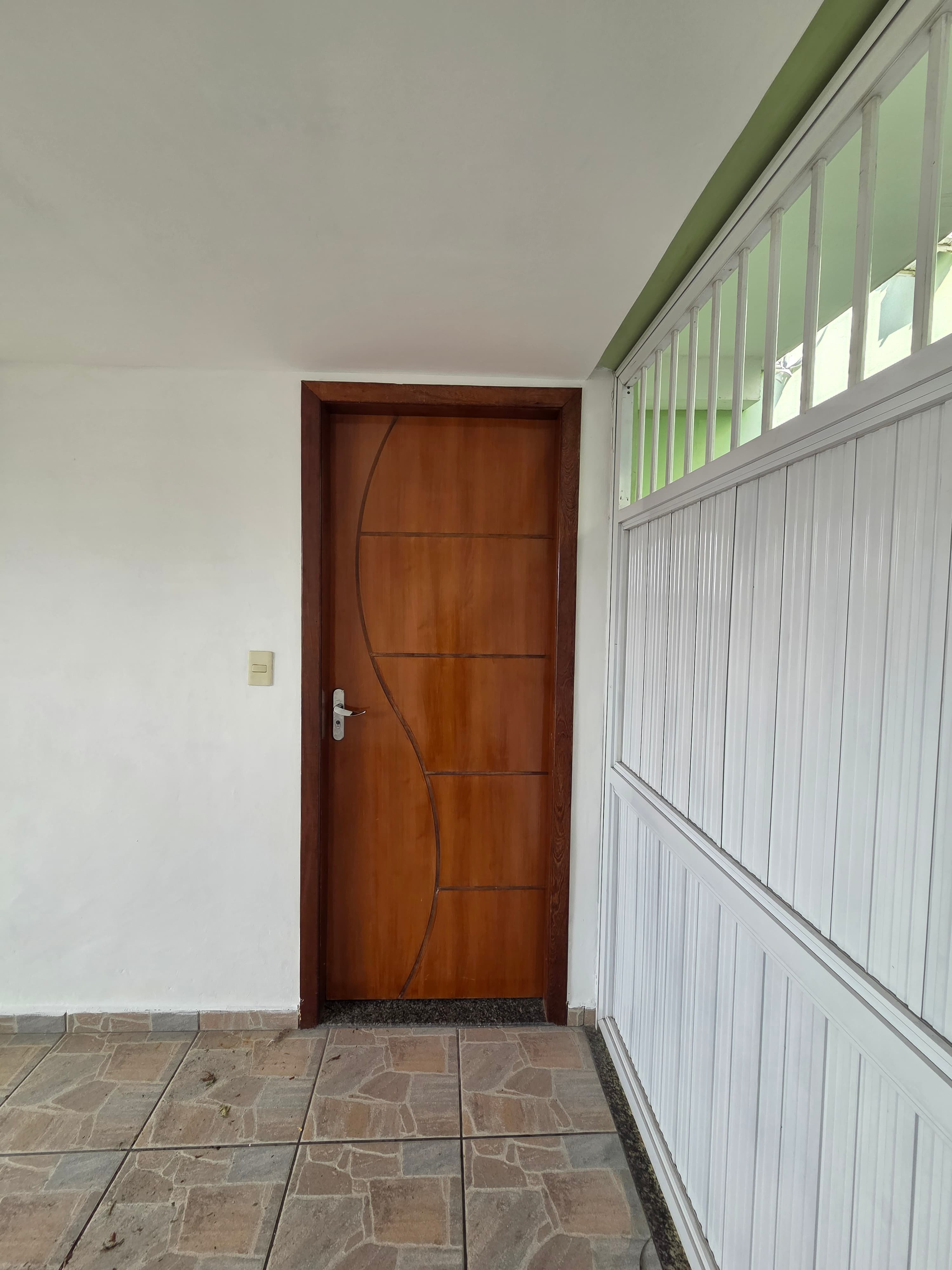 Porta de entrada em madeira com detalhe curvo e piso ceramico