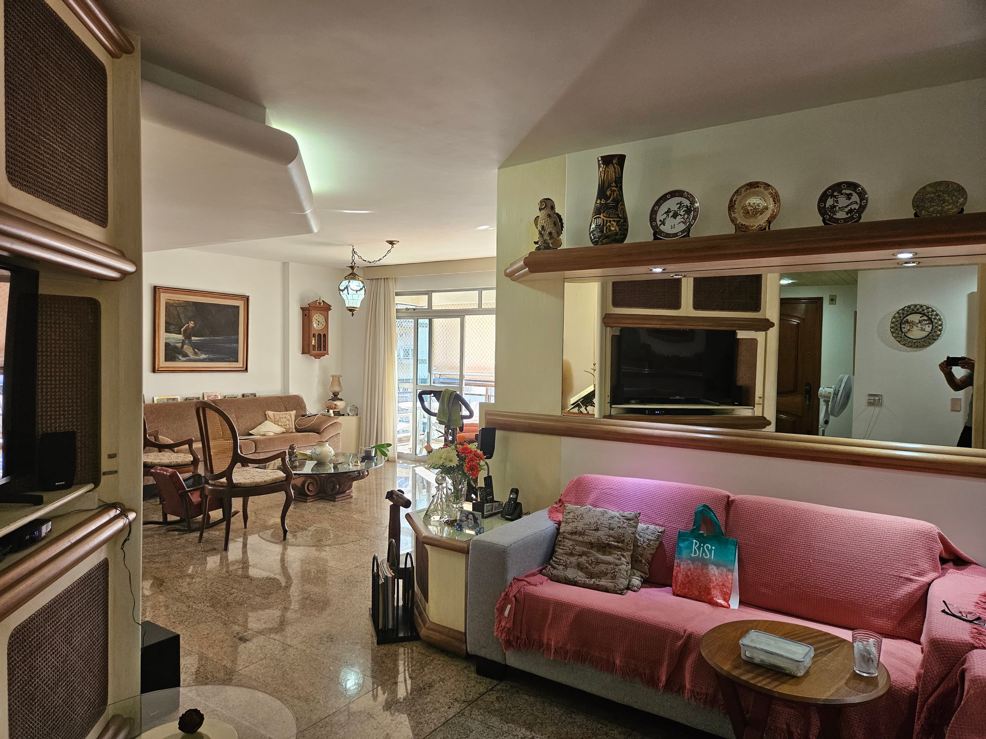 Sala de estar ampla com piso de granito, sofá rosa e parede espelhada com prateleira.