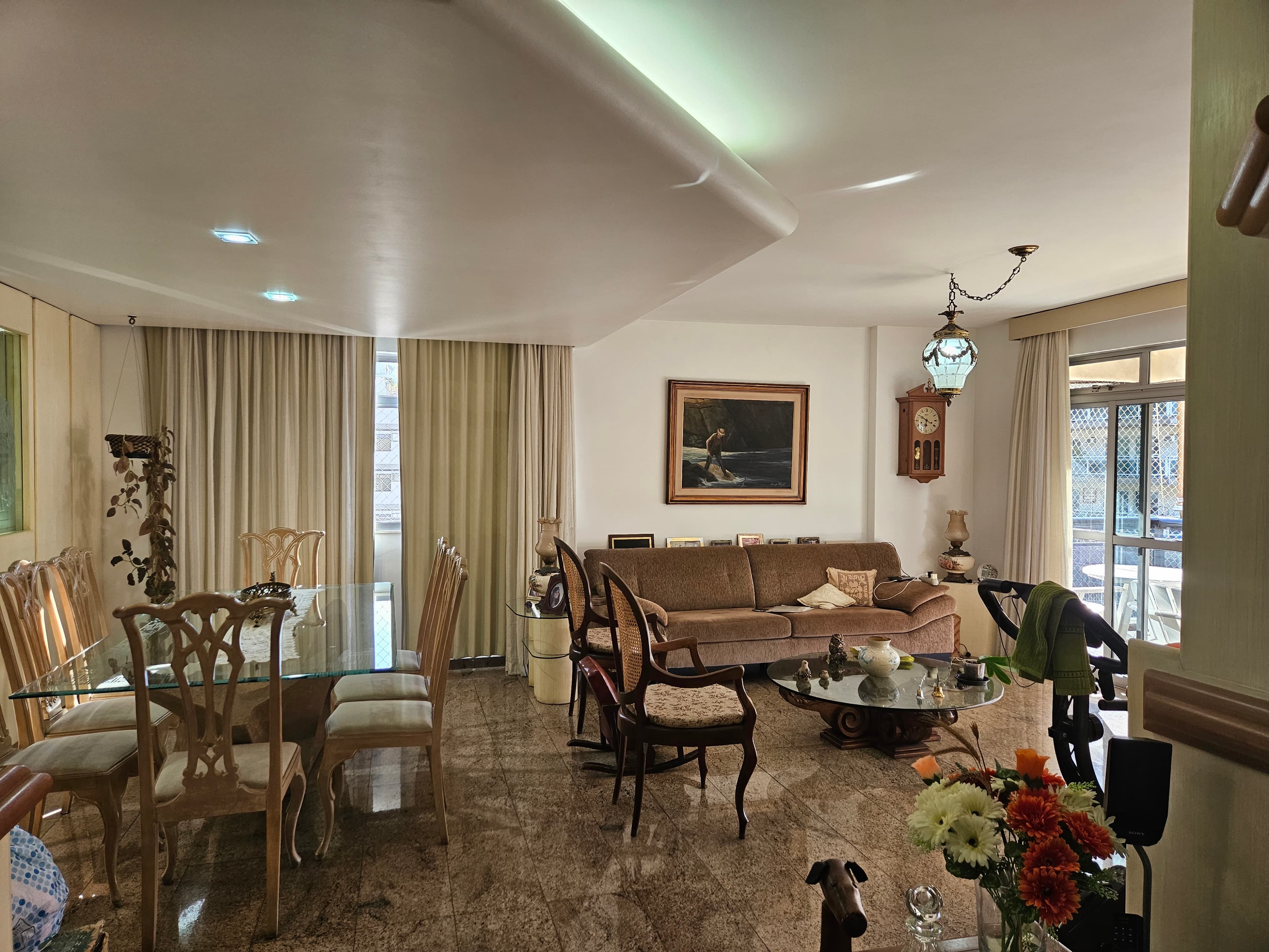 Sala integrada com estar e jantar, mesa de vidro com cadeiras clássicas e piso em granito.