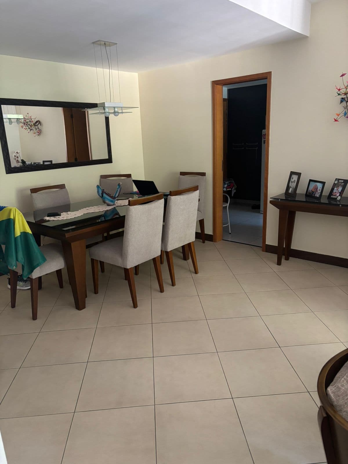 Sala de jantar integrada com mesa de madeira, seis cadeiras estofadas, espelho na parede e porta de acesso a outro ambiente.