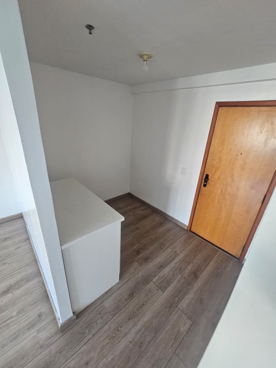 Sala comercial com piso amadeirado, paredes brancas e porta de madeira.
