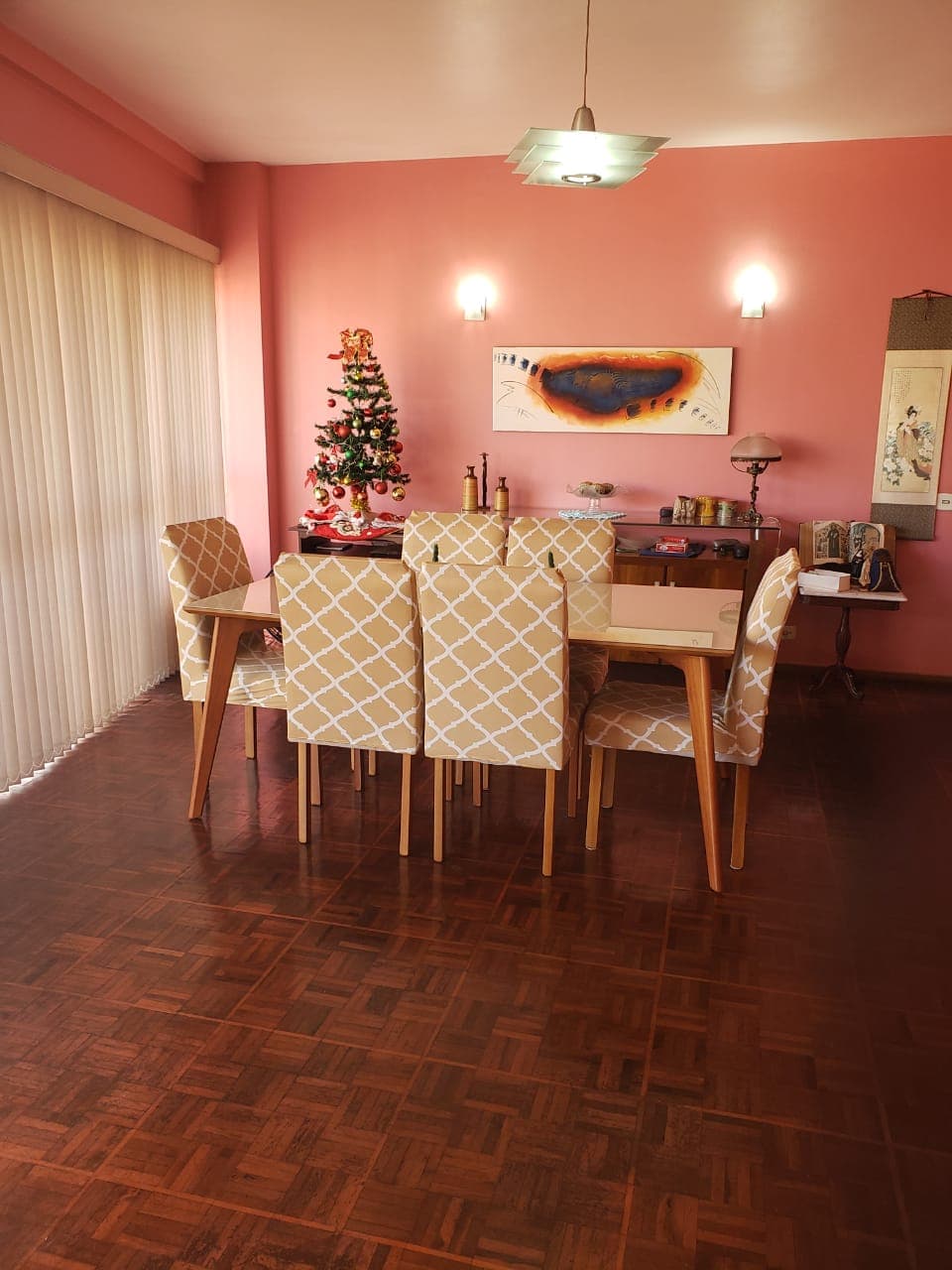 Sala de jantar integrada com piso de madeira escura, mesa com cadeiras revestidas e parede cor de rosa.